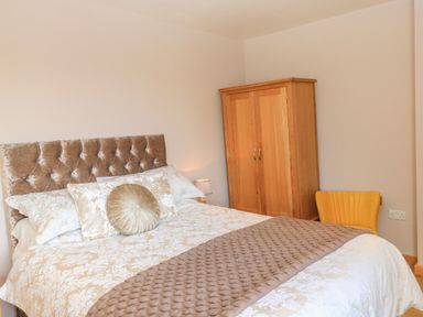 A bedroom with a bed that has patterned bedding and cushions a wooden wardrobe and a yellow chair at The Mews in Bovey Tracey near Chudleigh Knighton