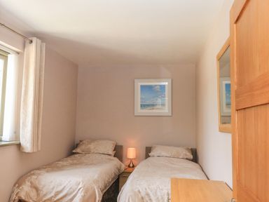 A bedroom with two single beds a nightstand with a lamp a window with curtains a framed picture and a mirror on the wall at The Mews in Bovey Tracey near Chudleigh Knighton