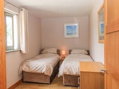 A bedroom with two single beds a bedside table with a lamp a window with curtains a wooden chest of drawers and a framed picture on the wall at The Mews in Bovey Tracey near Chudleigh Knighton