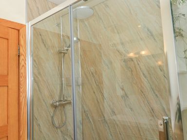 A shower area with a glass door wooden door and marble walls at The Mews in Bovey Tracey near Chudleigh Knighton