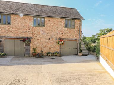 Exterior of a brick building with green window frames and two double doors with plants and flowers outside and a staircase on the right side at The Mews in Bovey Tracey near Chudleigh Knighton