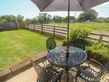 A garden patio with metal table and chairs a bottle of wine and glass on the table under an umbrella at The Mews in Bovey Tracey near Chudleigh Knighton