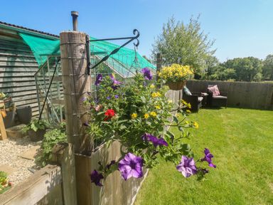 A garden with hanging flower pots and outdoor seating at The Mews in Bovey Tracey near Chudleigh Knighton