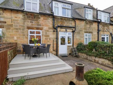 An outdoor patio area with a table and four chairs next to a stone house at Maypole Cottage in Fylingthorpe