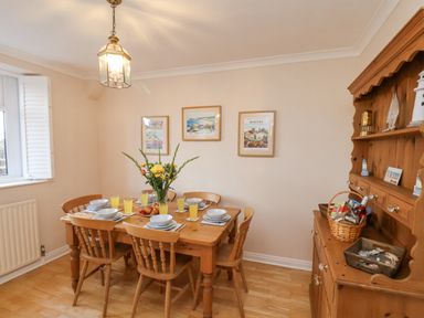 A dining room with wooden table set with plates glasses and croissants and wooden cabinet with basket at Maypole Cottage in Fylingthorpe