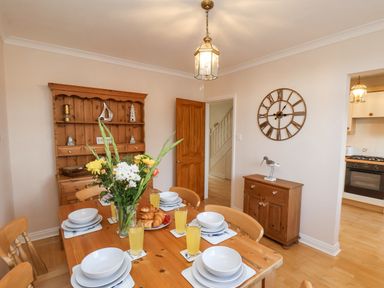 A dining room with a wooden table set with plates bowls glasses of juice and flowers at Maypole Cottage in Fylingthorpe