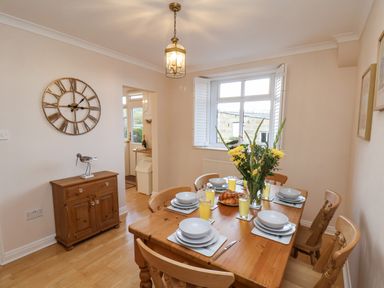 A dining room with a wooden table set with dishes and glasses and a window at Maypole Cottage in Fylingthorpe