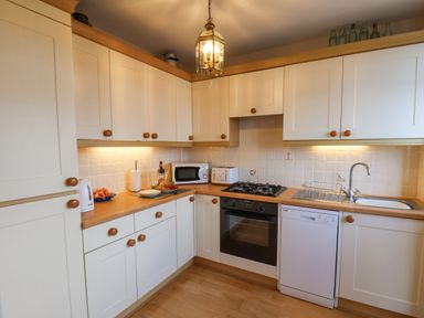 A kitchen with white cabinets wooden knobs a gas stove oven microwave dishwasher and a sink at Maypole Cottage in Fylingthorpe