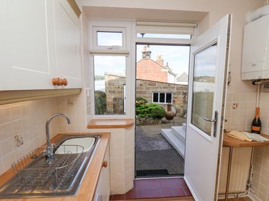 A kitchen with a sink and dish rack a door open to a patio at Maypole Cottage in Fylingthorpe