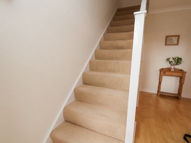A carpeted staircase next to a small wooden table with a vase of flowers on a wooden floor at Maypole Cottage in Fylingthorpe