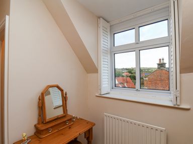 A small room with a wooden dressing table and mirror next to a window with white shutters at Maypole Cottage in Fylingthorpe