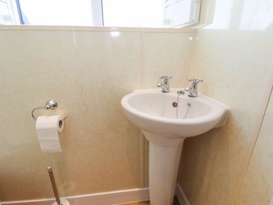 A bathroom sink with two taps and a toilet paper holder with a roll of toilet paper at Maypole Cottage in Fylingthorpe