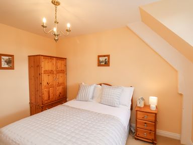 A bedroom with a double bed white bedding wooden wardrobe and wooden bedside table with lamp at Maypole Cottage in Fylingthorpe