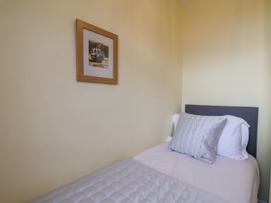 A single bed with white and gray bedding and a framed picture of a boat on the wall at Maypole Cottage in Fylingthorpe