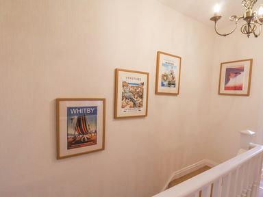 A hallway wall with four framed coastal posters and a white wooden banister at Maypole Cottage Fylingthorpe