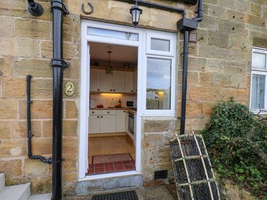 An open door showing a kitchen with white cabinets and wooden knobs in a stone building at Maypole Cottage in Fylingthorpe
