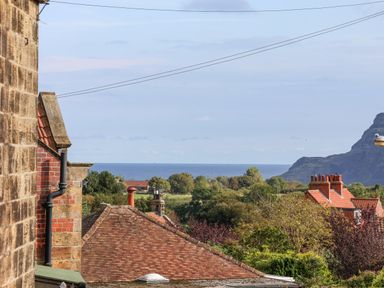 A view of rooftops trees sea and hills from a window at Maypole Cottage in Fylingthorpe