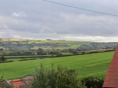 A rural landscape with green fields trees and rooftops under a cloudy sky at Maypole Cottage in Fylingthorpe