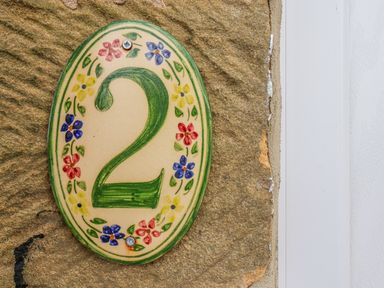 A ceramic house number 2 plaque with painted flowers on a stone wall next to a white door frame at Maypole Cottage in Fylingthorpe