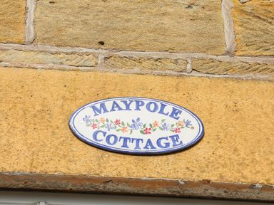A wall with a Maypole Cottage sign with flowers in Fylingthorpe