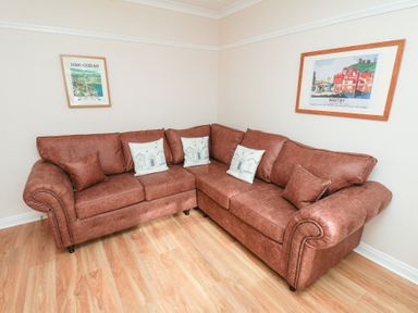 A living room with a corner sofa and framed pictures at Maypole Cottage in Fylingthorpe