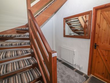 A wooden staircase with striped carpet next to a wooden door and a wall mirror at Swallows Retreat Carew
