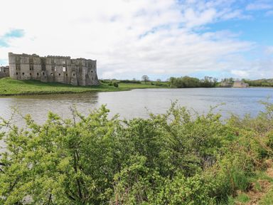 A body of water with green bushes in the foreground a large stone castle on the left and buildings on the right at Swallows Retreat in Carew
