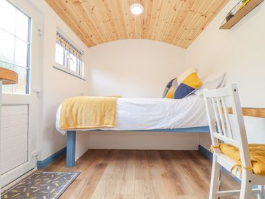 A small bedroom with a bed a white chair a desk and a wooden ceiling at Sunflower Sparnon Gate near Illogan