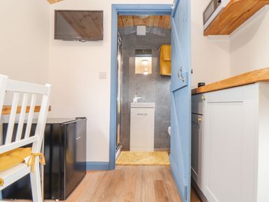 A small kitchen area with a white chair and mini fridge a blue door leading to a bathroom at Sunflower Sparnon Gate near Illogan