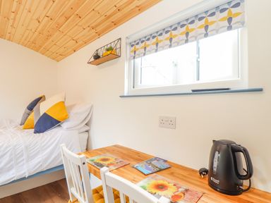 A small room with a bed, a wooden table with two white chairs, a window with patterned blinds, and a black electric kettle on the table at Sunflower Sparnon Gate near Illogan
