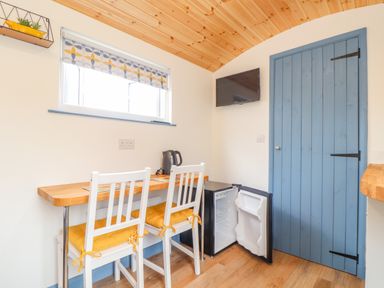 A small dining area with two white chairs and a wooden table a blue door and a small open fridge on the floor at Sunflower Sparnon Gate near Illogan