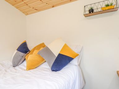 A bed with three decorative pillows and a small shelf with plants on a wall at Sunflower Sparnon Gate near Illogan