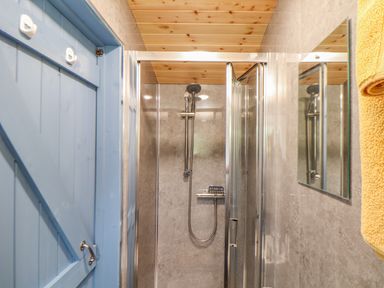 A bathroom with a blue wooden door a shower with glass doors a wooden ceiling and a yellow towel at Sunflower Sparnon Gate near Illogan