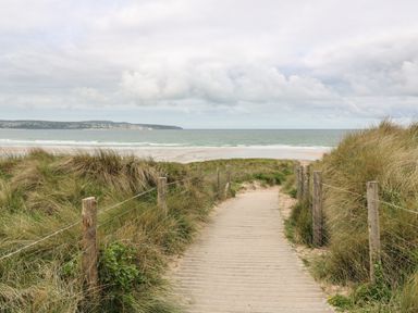 A wooden pathway between grassy sand dunes leading to a beach and ocean at Sunflower Sparnon Gate near Illogan