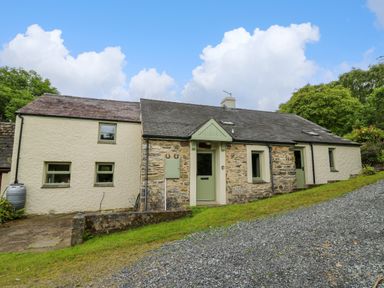 A stone and plaster house with green doors and windows along a gravel driveway at Taibach in Dinas Cross