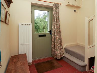 An entrance hallway with a green door a curtain stairs with gray carpet and a wooden bench at Taibach in Dinas Cross