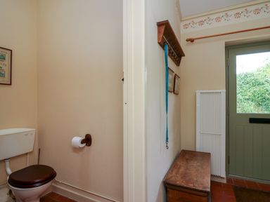 A small room with a toilet and toilet paper holder connected to a hallway with a wooden bench door with a window and a coat rack with hooks and a blue strap at Taibach in Dinas Cross