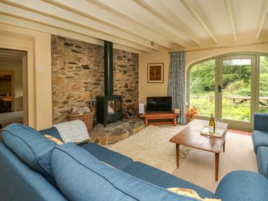A living room with blue sofas a wood stove and a wooden coffee table in front of glass doors at Taibach in Dinas Cross