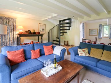A living room with blue sofas and a wooden coffee table with wine and glasses near a black spiral staircase at Taibach in Dinas Cross