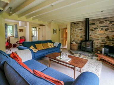 A living room with blue sofas a wooden coffee table stone fireplace and wood stove at Taibach in Dinas Cross