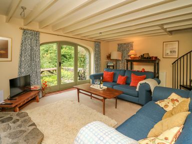 A living room with blue sofas and a wooden coffee table near large arched glass doors at Taibach in Dinas Cross