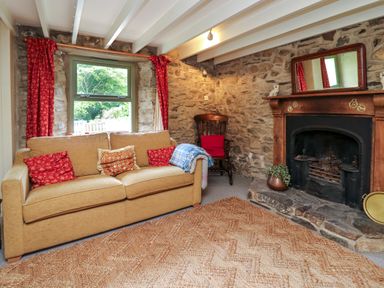 A sitting room with a sofa cushions wooden chair stone walls and a fireplace at Taibach in Dinas Cross