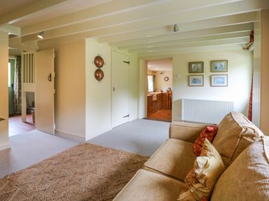 A living room with a beige sofa and cushions a woven rug on the floor copper pans on the wall and a view into a kitchen at Taibach in Dinas Cross