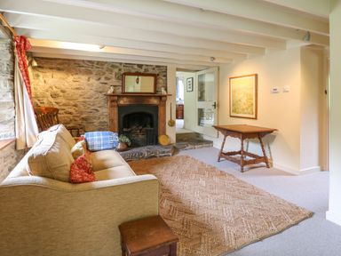 A living room with a sofa a rug a fireplace and a wooden table at Taibach in Dinas Cross