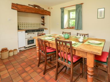 A kitchen with a wooden dining table set with plates and cups and a stove in an alcove at Taibach in Dinas Cross