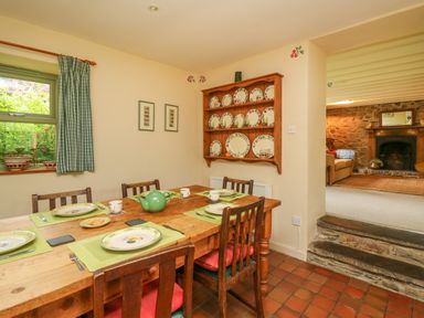 A dining room with wooden table and chairs set with plates cups and teapot adjacent to a living room with stone fireplace at Taibach in Dinas Cross