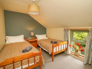 A bedroom with two single wooden beds a nightstand with a lamp and a window with curtains and flowers at Taibach in Dinas Cross