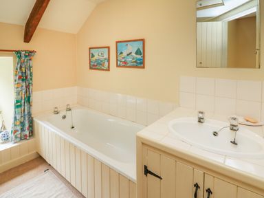 A bathroom with a bathtub sink mirror and window with patterned curtain at Taibach in Dinas Cross