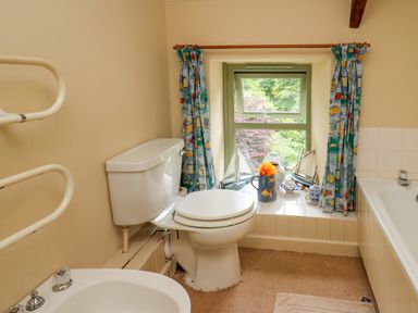 A bathroom with a toilet and bidet next to a window with curtains and decorative items on the windowsill at Taibach in Dinas Cross