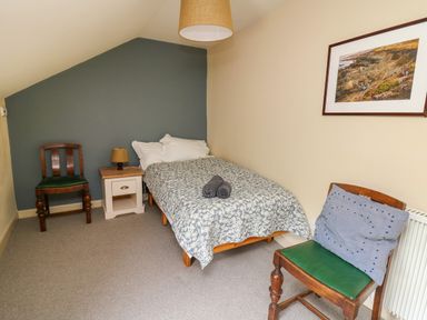 A bedroom with a single bed two wooden chairs a nightstand with a lamp and a framed picture on the wall at Taibach in Dinas Cross